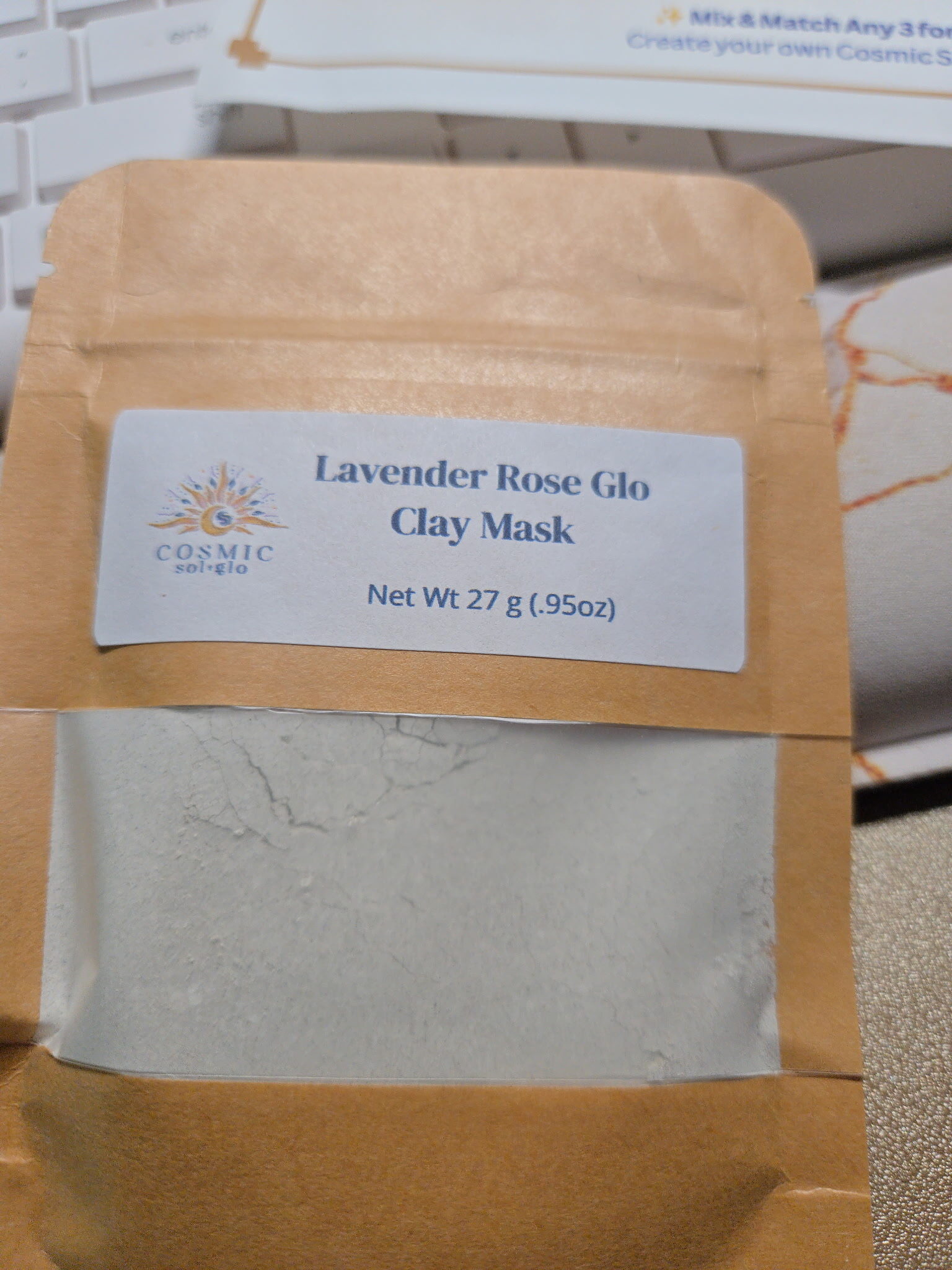 Nebula Honey Glo and Lavender Rose Glo clay mask pouches styled with pink flowers and gold glitter
